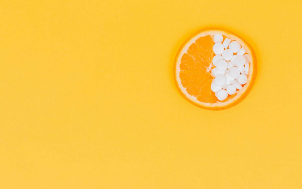 Orange slice, half covered with vitamins on a yellow background 