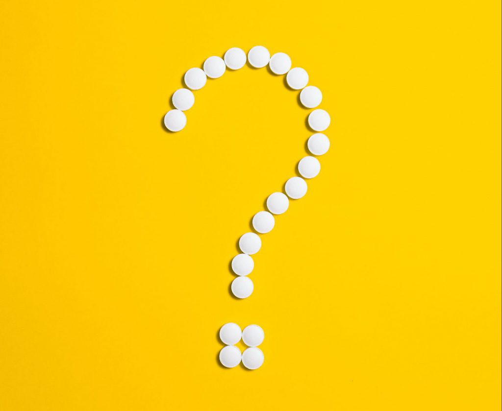 White pills in shape of a question mark on a yellow background 
