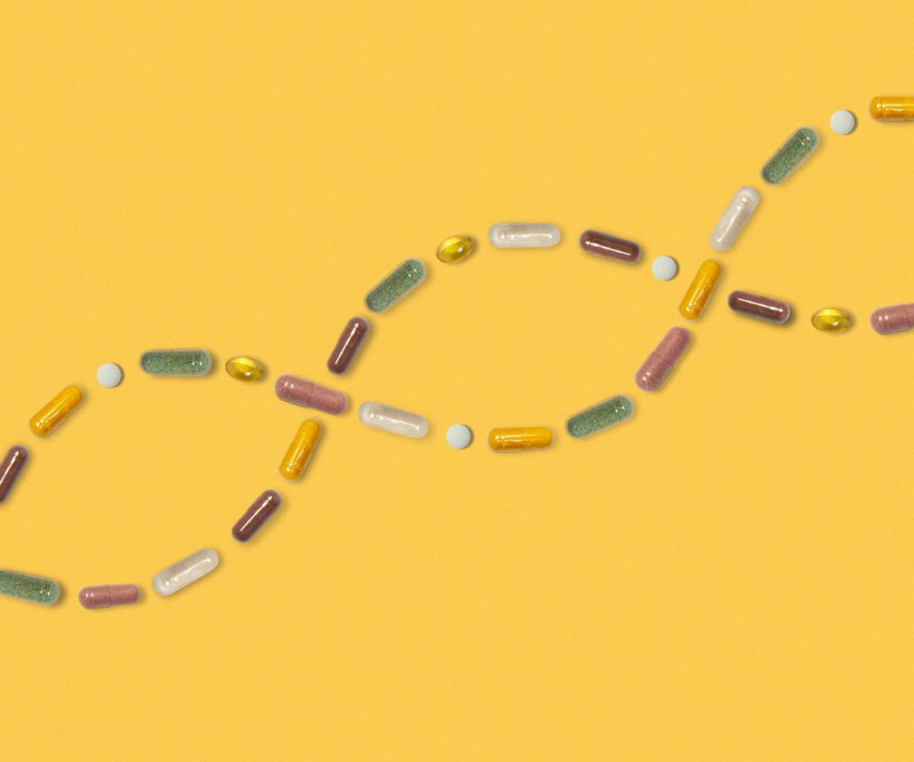 Multicoloured pills in curving lines like DNA on a yellow background