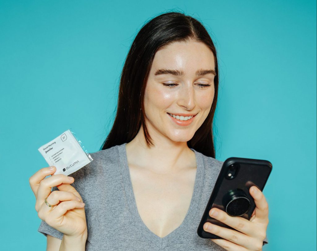 Women holding phone and Autumn pill package in either hand, blue background