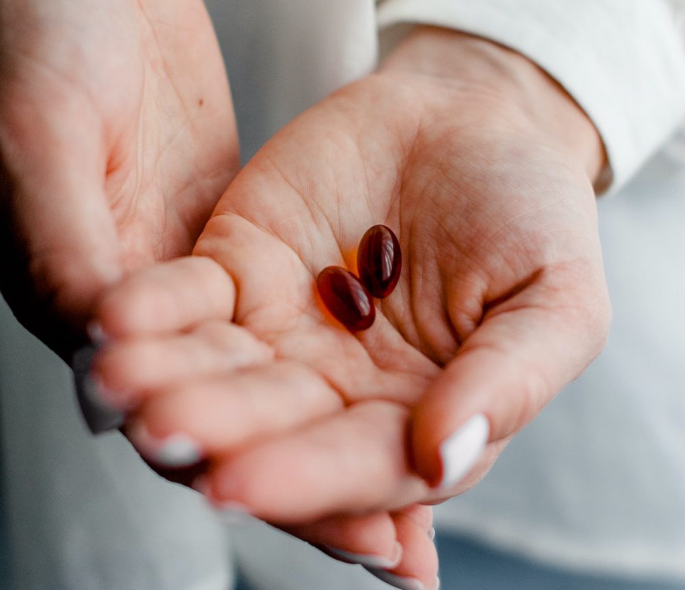 Two hands holding small red supplement capsules
