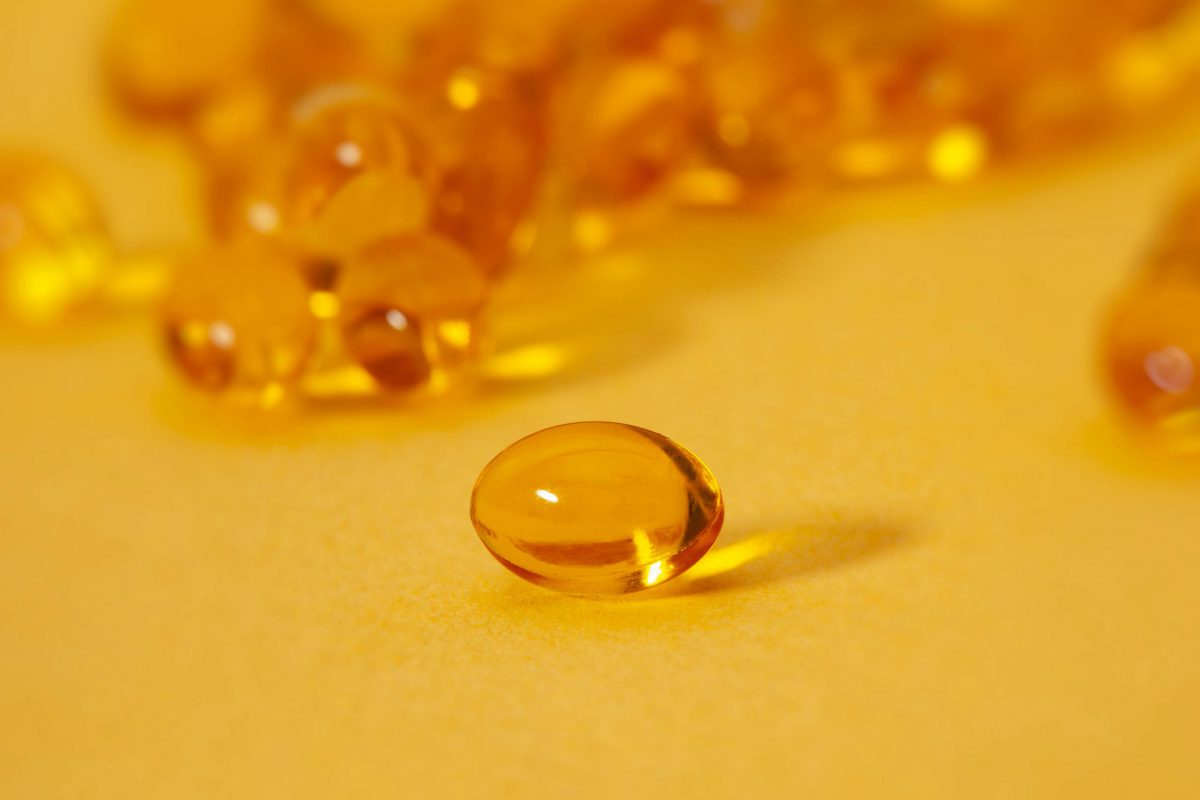 Brown pill capsule in focus on a yellow surface with several other brown capsules in the background