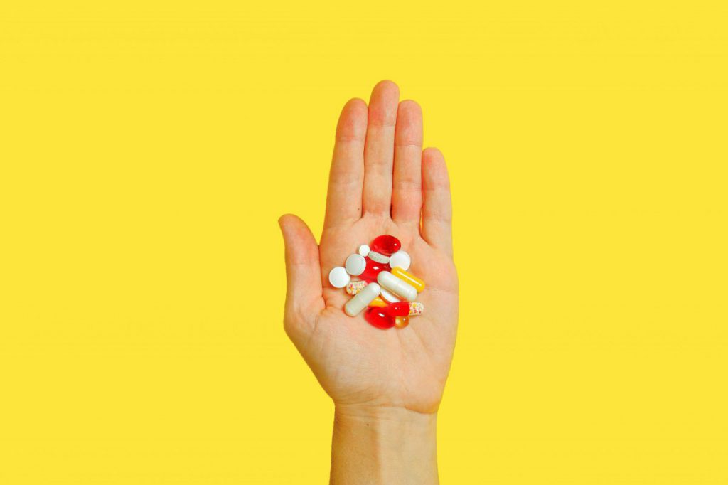 Yellow background with hand holding lots of multi-coloured pills
