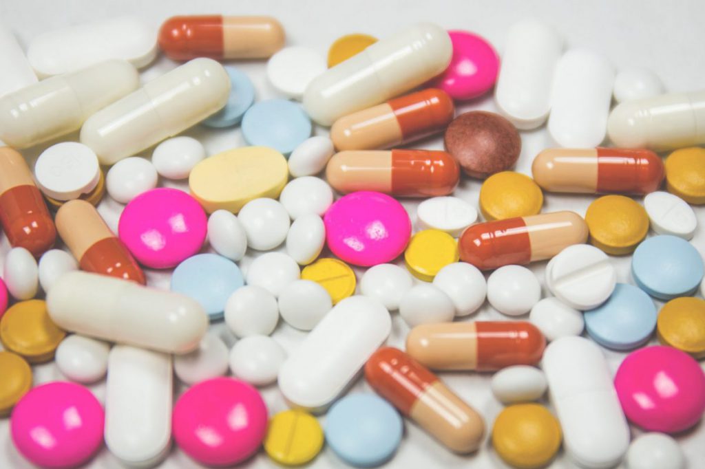 Multiple different kinds and colours of pills across plain background