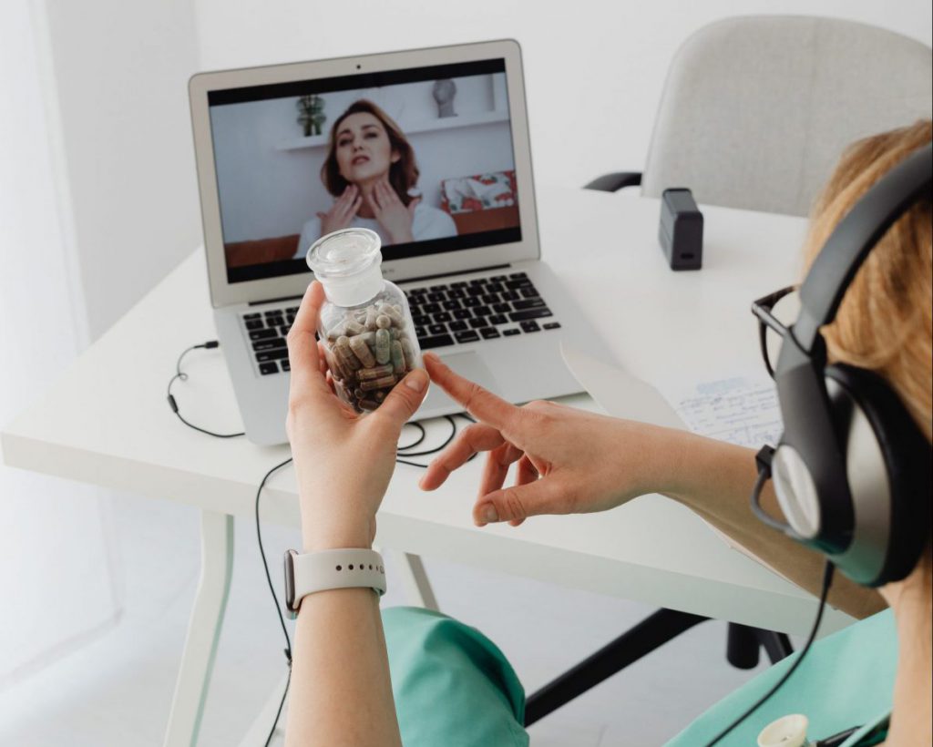 Patient on Zoom talking to doctor with jar of pills in hand