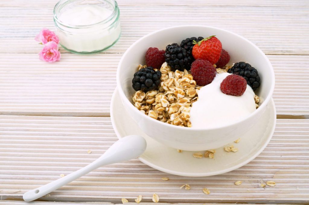 A white bowl of yogurt topped with berries and granola on a table