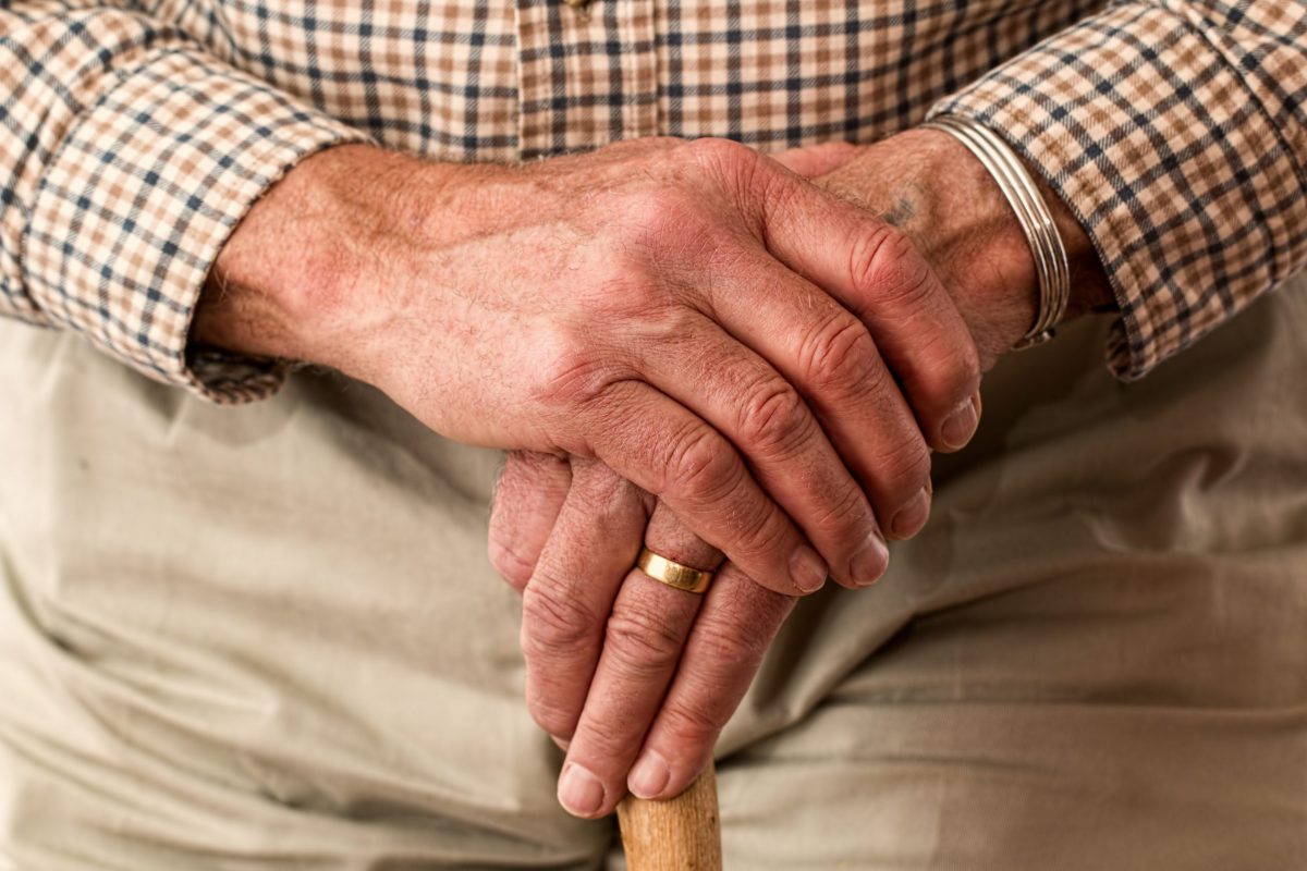 Elderly man leaning two hands on a cane.