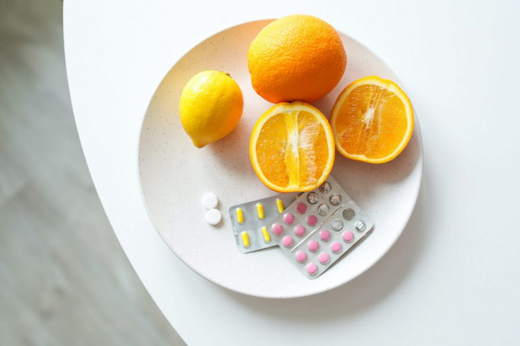 Plate on table with oranges, lemon and two pill packs on it
