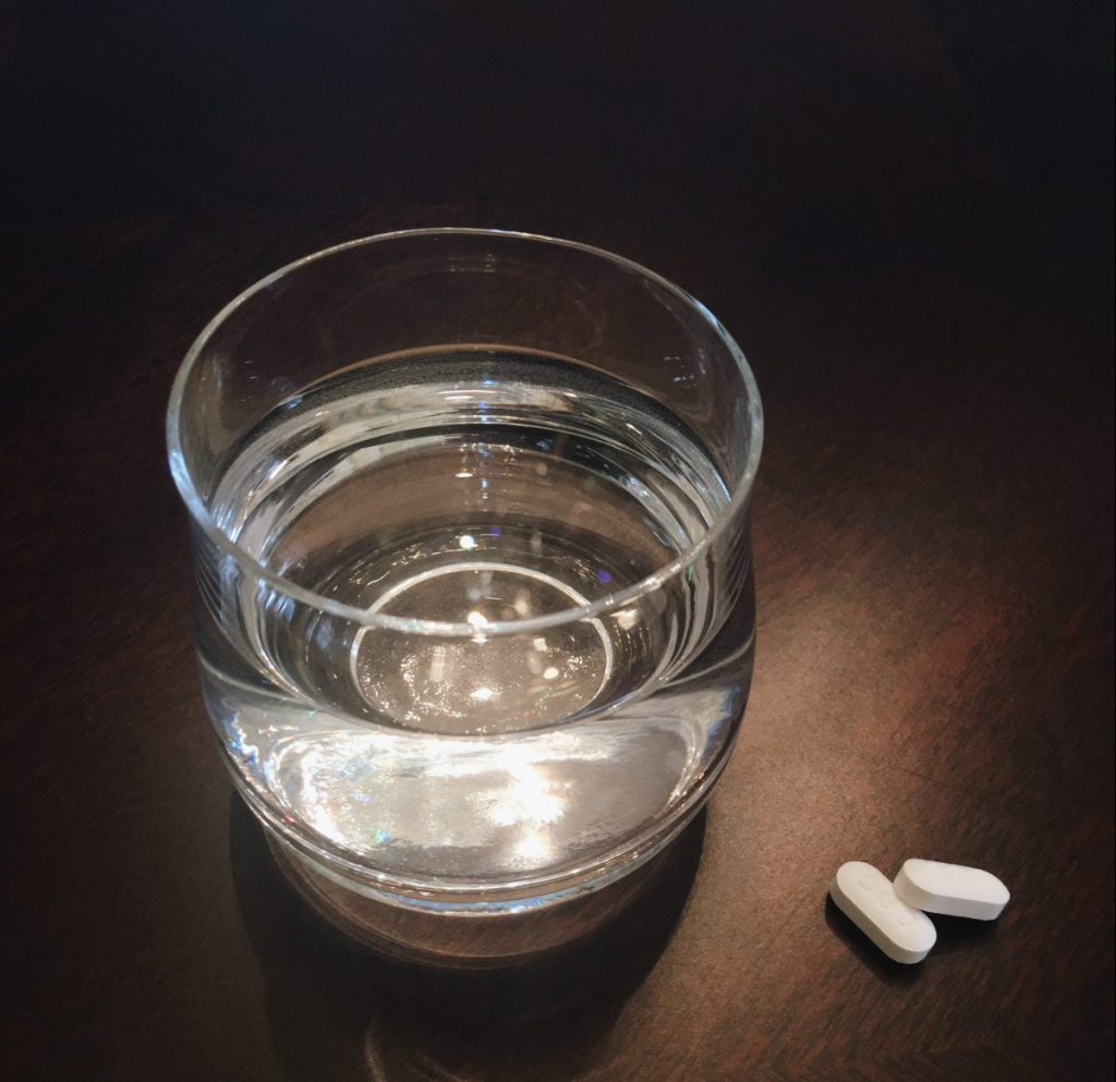 Glass of water on wooden desk with two white pills 