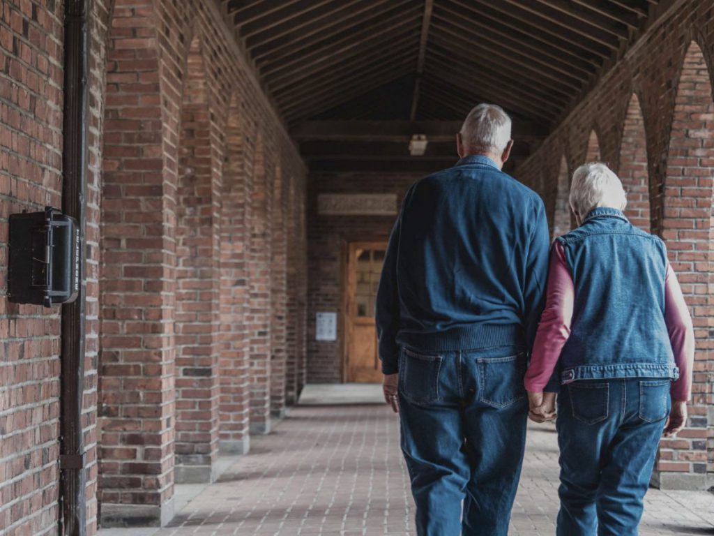 Elderly couple walking down a brick-covered hallway.