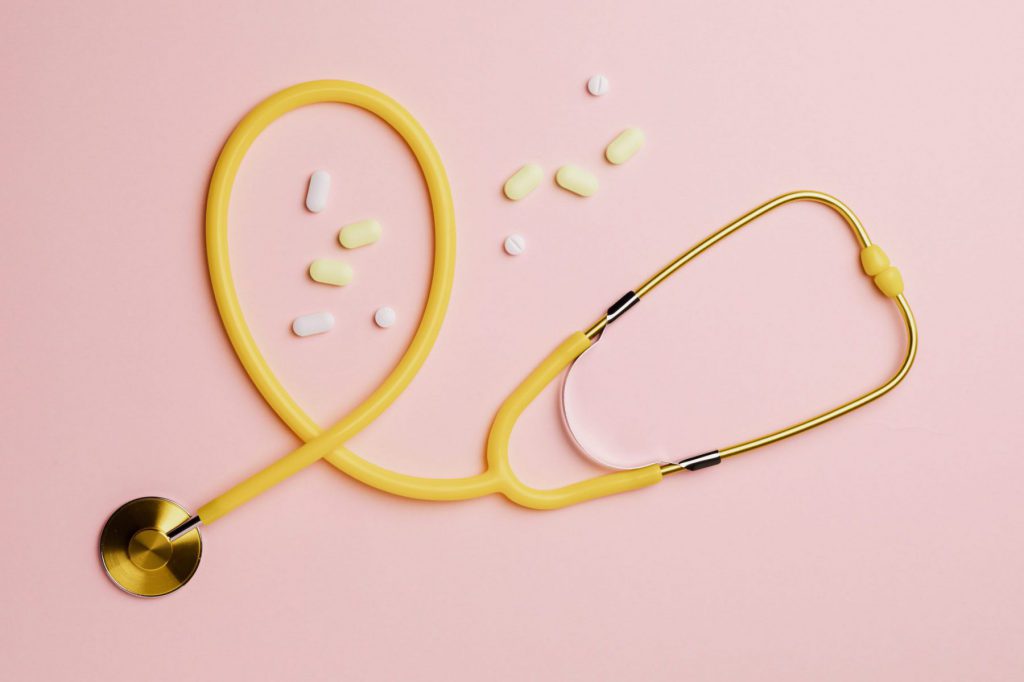 Vitamins beside a yellow stethoscope on a pink background