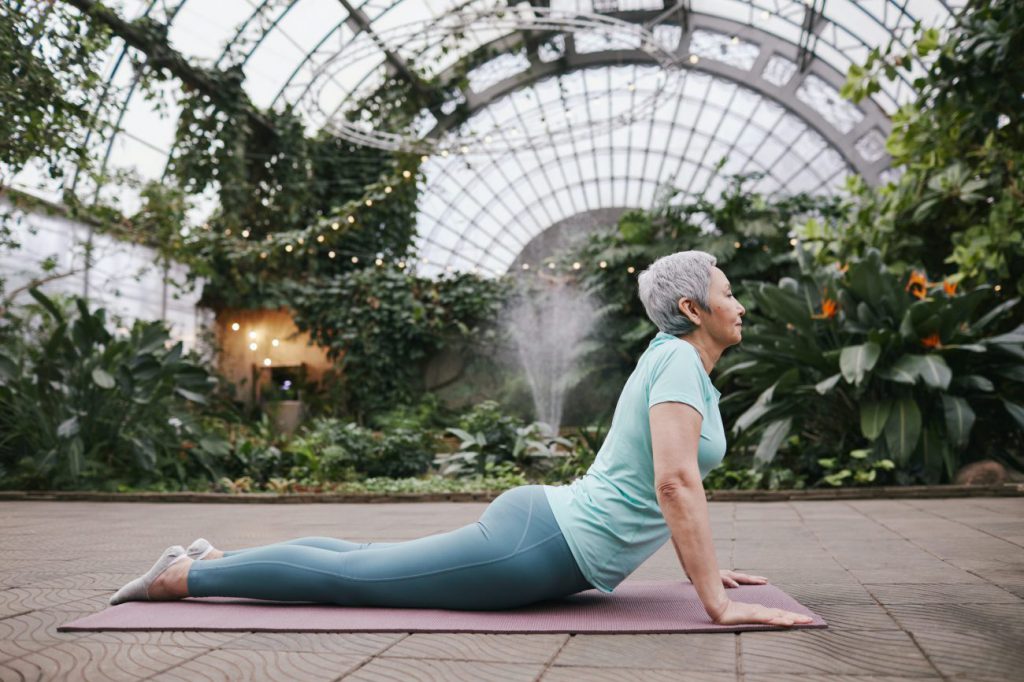 elderly woman doing yoga in a greenhouse.