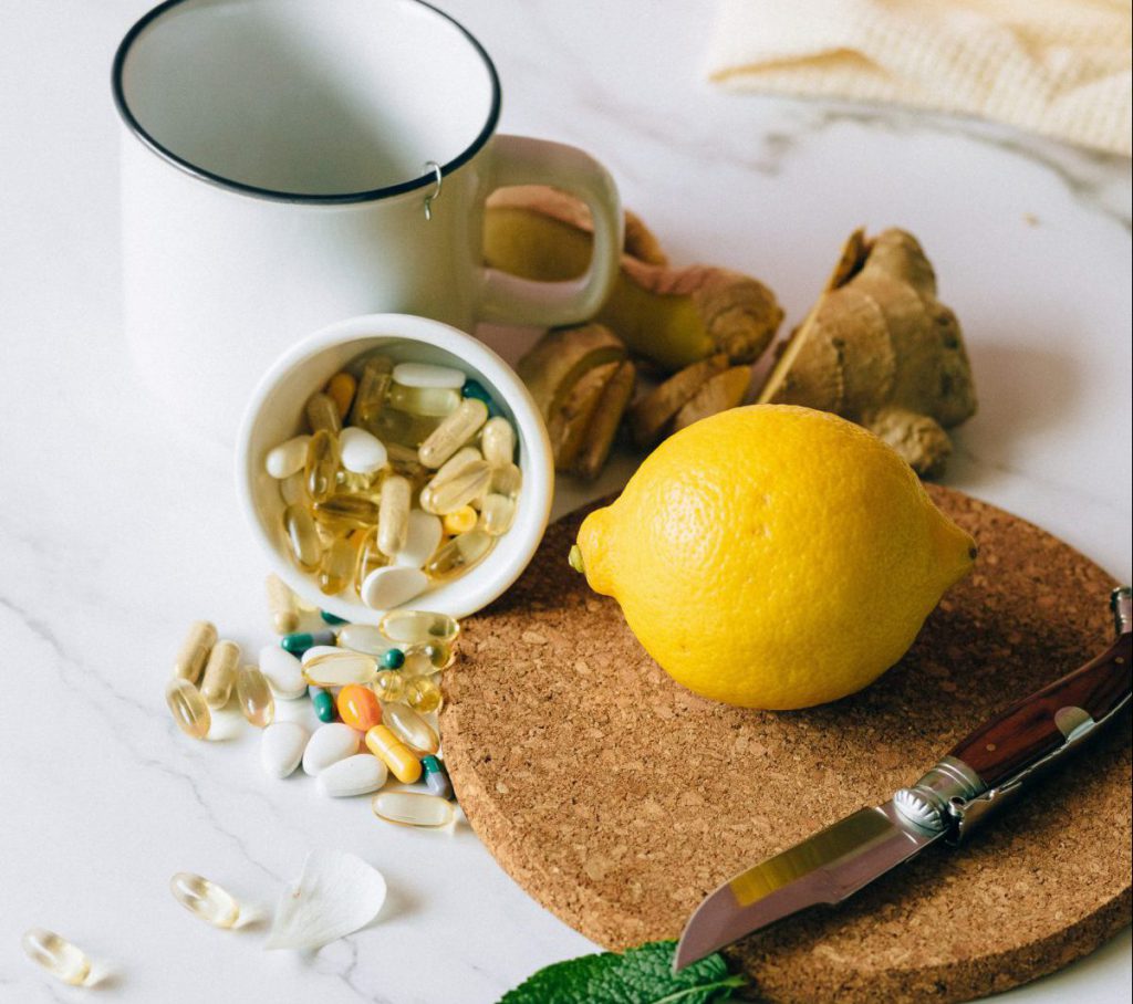 Cutting board with lemon and ginger, a mug and cup of vitamins and supplements falling out