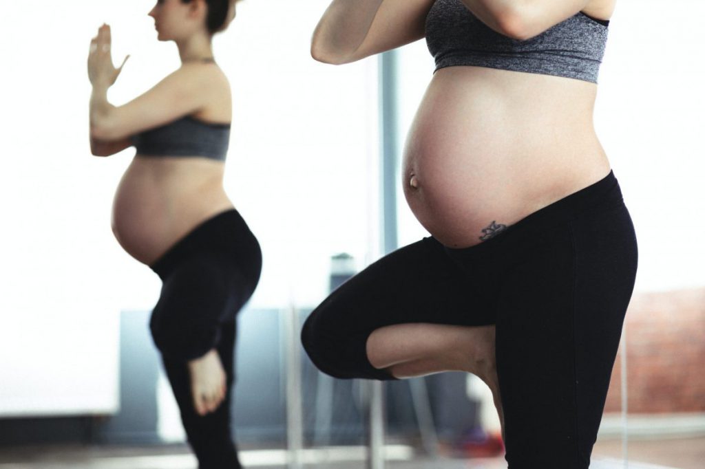 Pregnant woman standing in the mirror doing yoga.