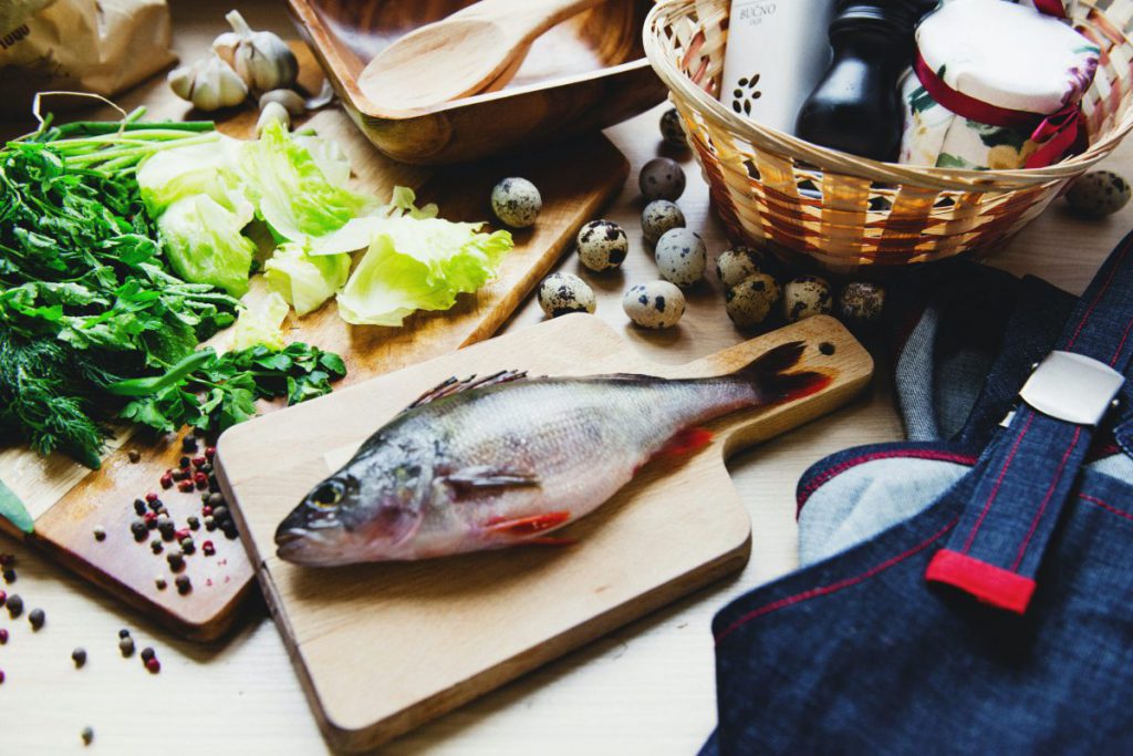 Raw fish on a cutting board surrounding other ingredients and kitchen utensils.