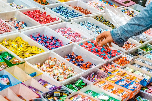 A large display of sweets at the grocery store with a person selecting pieces of candy.