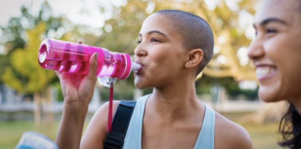 Woman drinking water from a refillable bottle while smiling